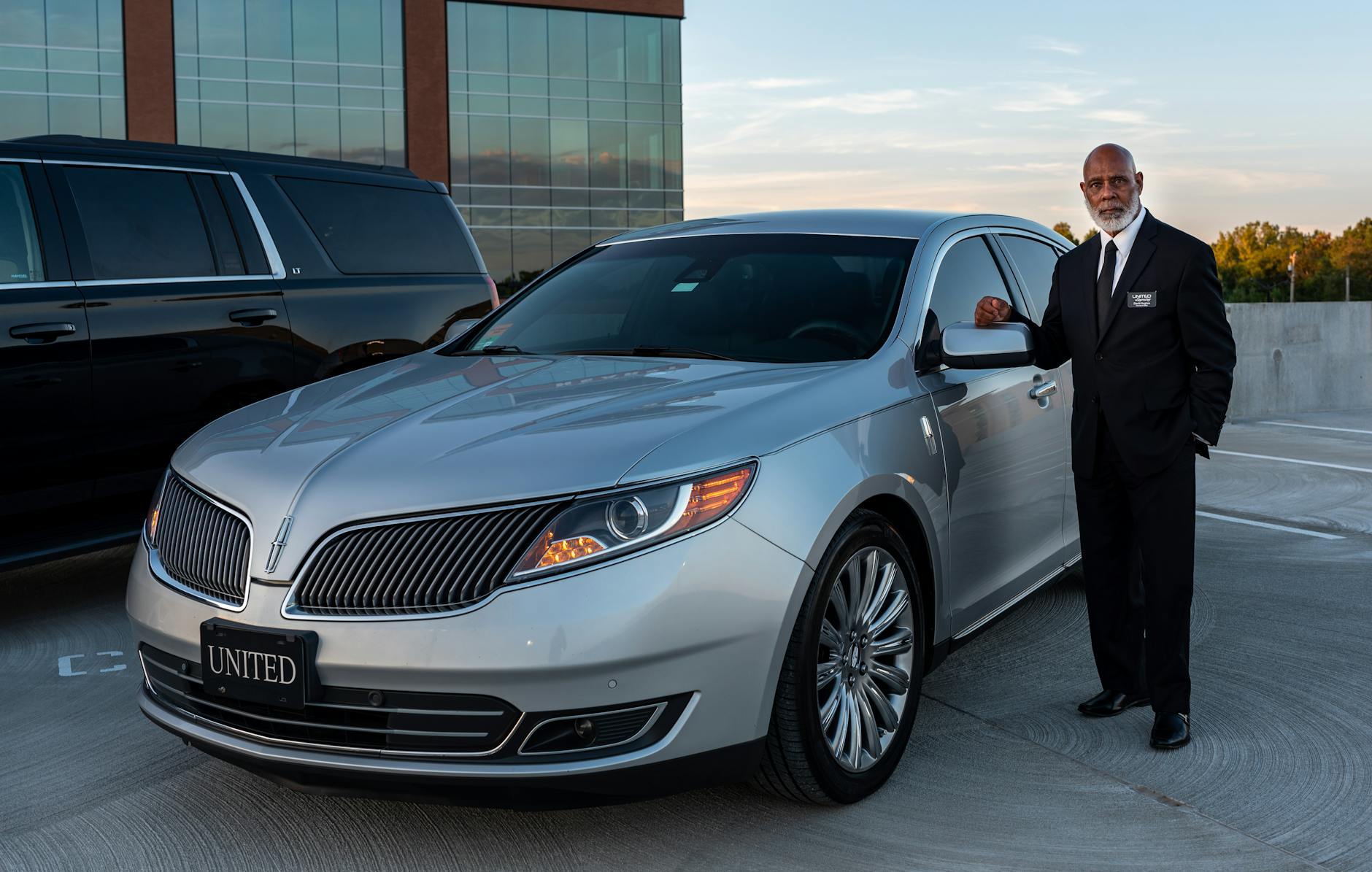 Professional chauffeur beside a black premium sedan, Volantis Limousine Services premium sedan class